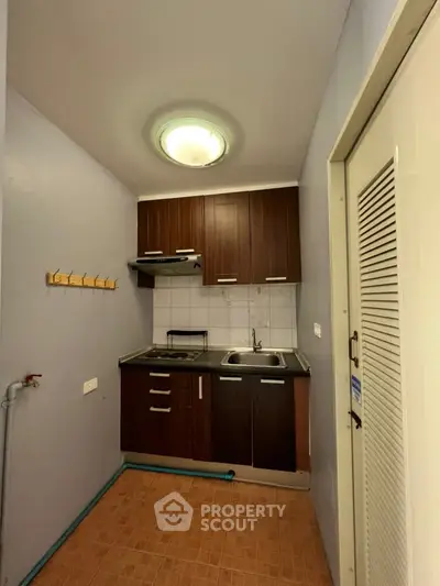 Compact kitchen with wooden cabinets and tiled backsplash in cozy apartment