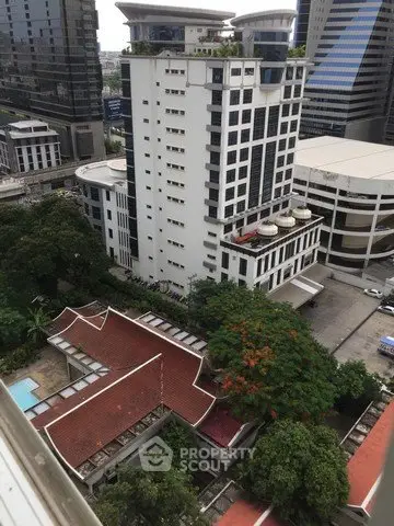 Stunning aerial view of modern high-rise building with lush greenery and traditional architecture in urban setting.