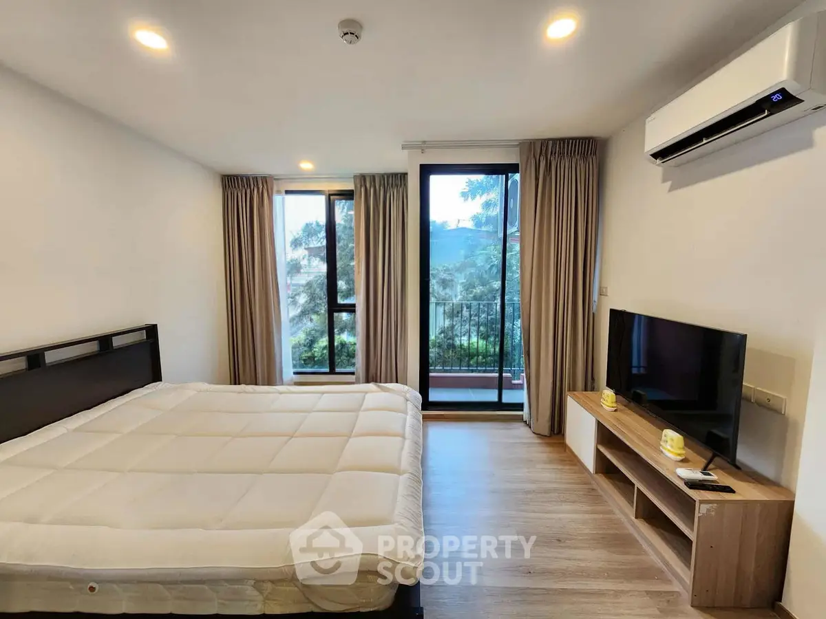 Spacious bedroom with large windows and balcony access, featuring modern furnishings and a serene view.