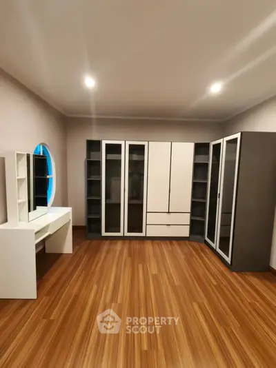 Spacious bedroom with modern wardrobe and elegant vanity set on wooden flooring.