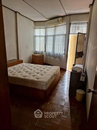 Cozy bedroom with natural light and parquet flooring, featuring a comfortable bed and minimalistic furniture.