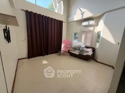Spacious room with high ceilings and large windows, featuring a cozy corner with a bed and air conditioning.