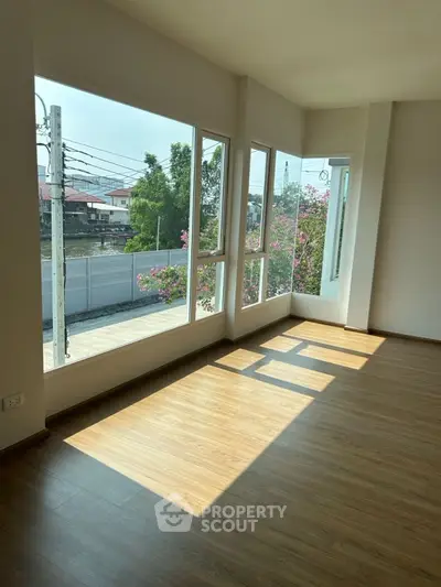 Bright corner unit with large windows and wooden flooring, offering a serene view of greenery.