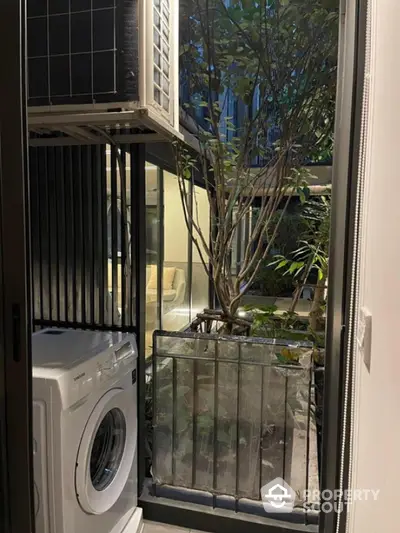 Modern apartment balcony with washing machine and lush greenery