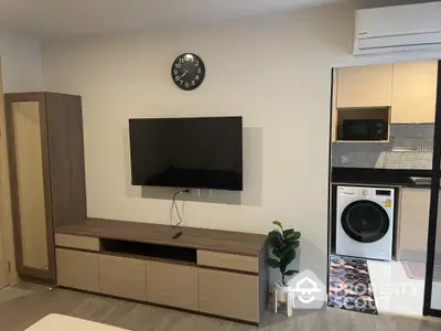 Modern living room with wall-mounted TV and adjacent kitchen area featuring washing machine.