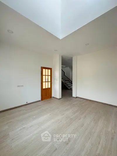 Spacious empty room with wooden flooring and staircase, perfect for customization.