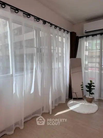 Bright room with large windows, sheer curtains, and a stylish mirror reflecting natural light.