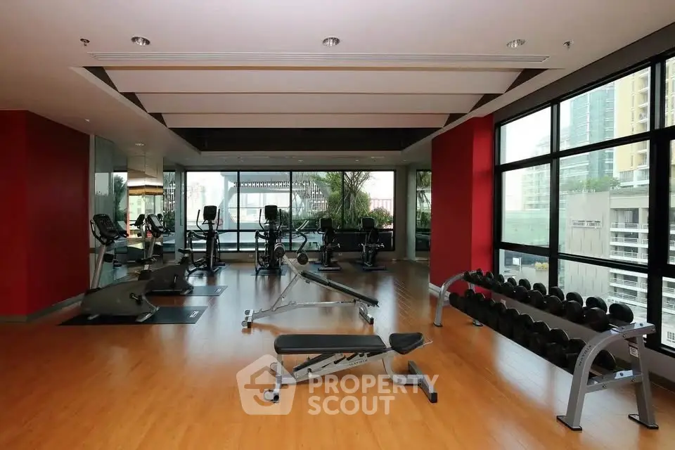 Spacious gym with modern equipment and city view in luxury apartment building.