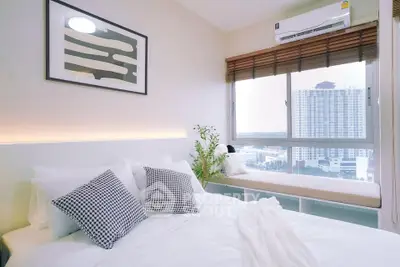 Modern bedroom with large window and city view, featuring stylish decor and cozy seating area.