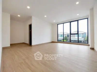 Spacious empty living room with large windows and wooden flooring in modern home.