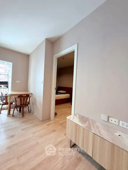Modern apartment interior with wooden flooring, dining area, and bedroom entrance.