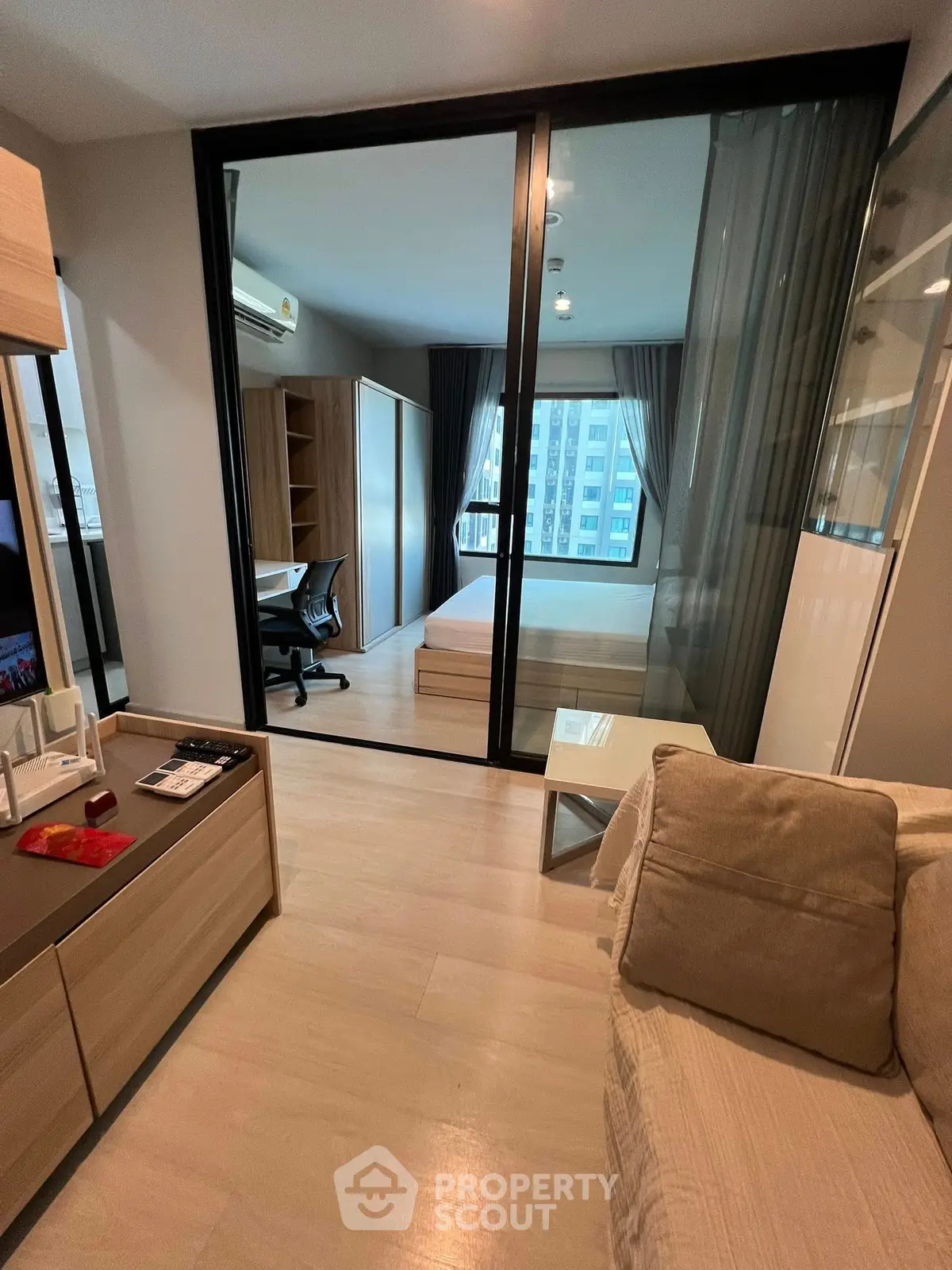 Modern apartment with open living room and bedroom, featuring sleek furniture and large windows.