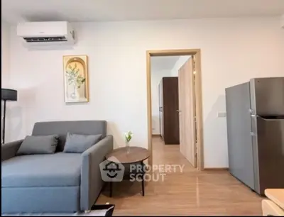 Modern living room with gray sofa, air conditioner, and sleek refrigerator