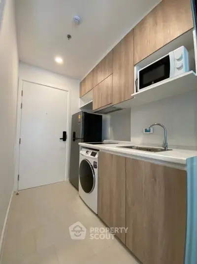Modern kitchen with sleek wooden cabinets, washing machine, and microwave in a compact layout.