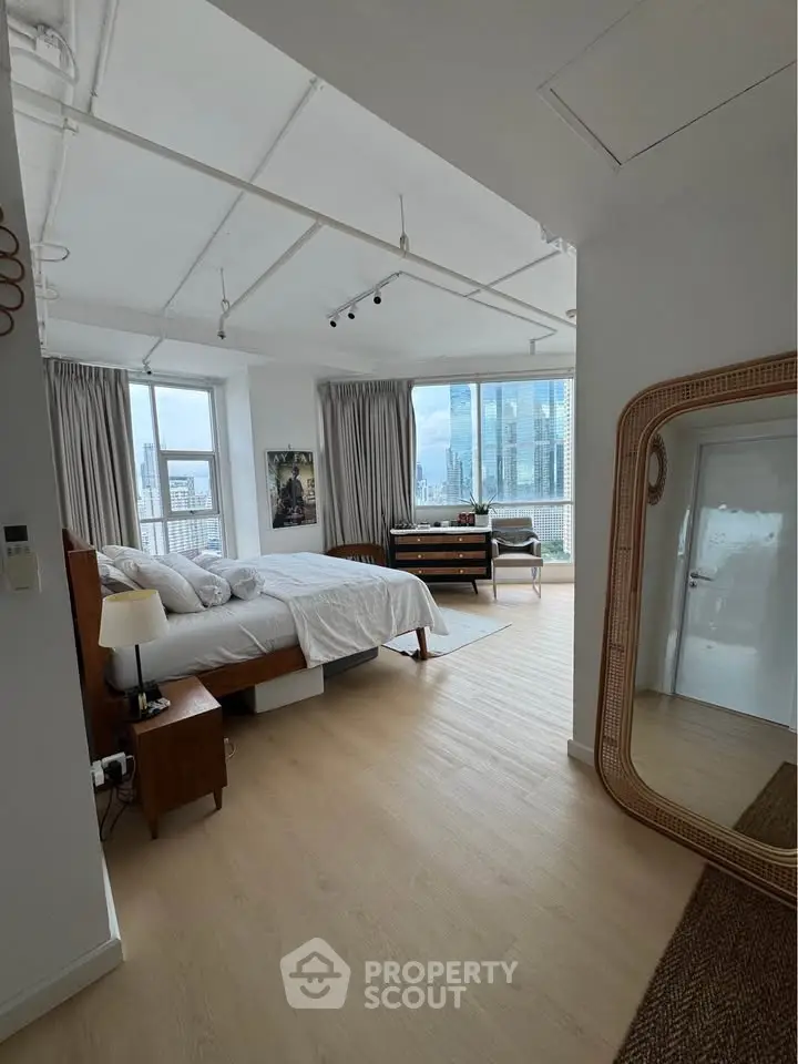 Spacious bedroom with city view, modern decor, and large windows in a high-rise apartment.