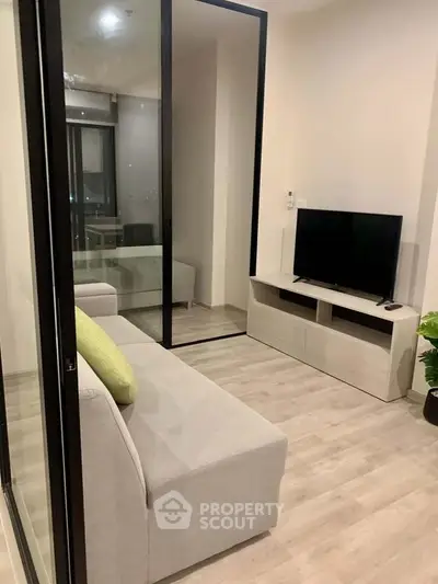 Modern living room with sleek design and glass partition, featuring a cozy sofa and flat-screen TV.