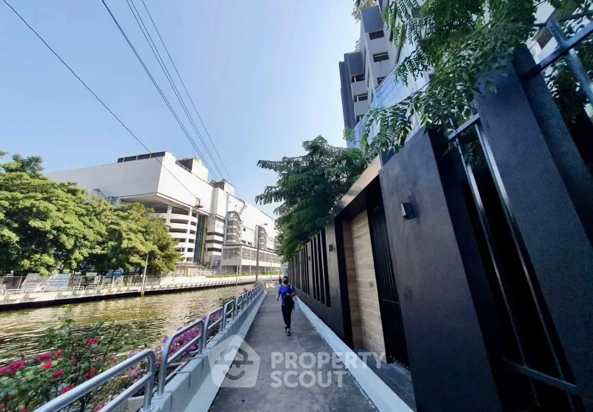Scenic canal-side walkway with modern buildings and lush greenery, perfect for urban living.