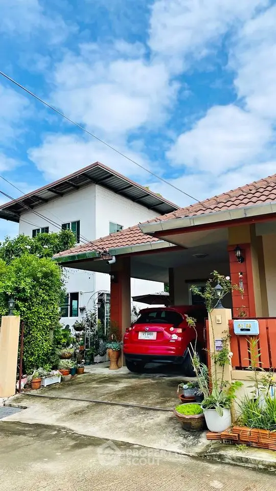 Charming two-story home with a covered carport and vibrant garden, showcasing a spacious driveway and a welcoming entrance under a clear blue sky.