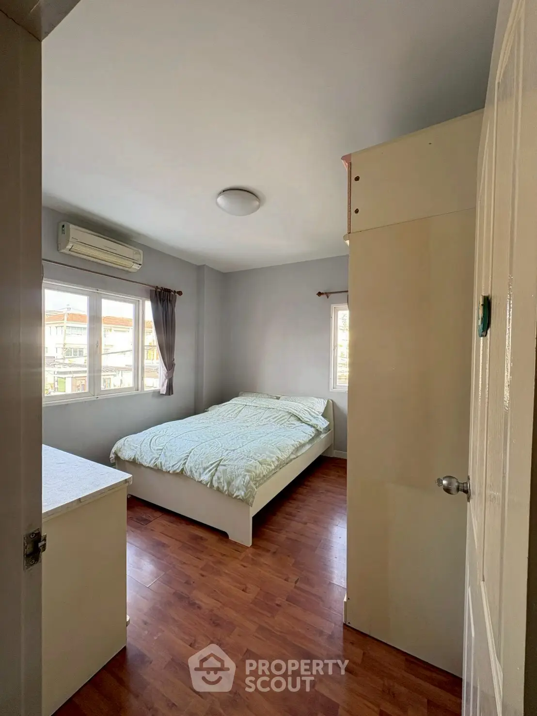 Cozy bedroom with wooden flooring and ample natural light, featuring a comfortable bed and air conditioning.