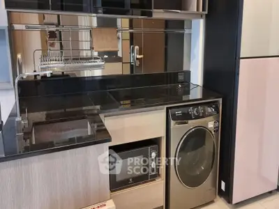 Modern kitchen with sleek appliances including washing machine and microwave, featuring elegant black countertops.