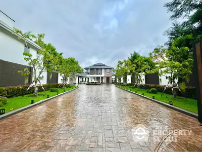 Elegant driveway leading to a luxurious mansion surrounded by lush greenery and manicured gardens.