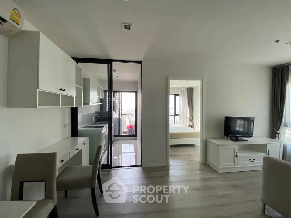 Modern apartment with open living area and kitchen, featuring sleek furniture and large windows.