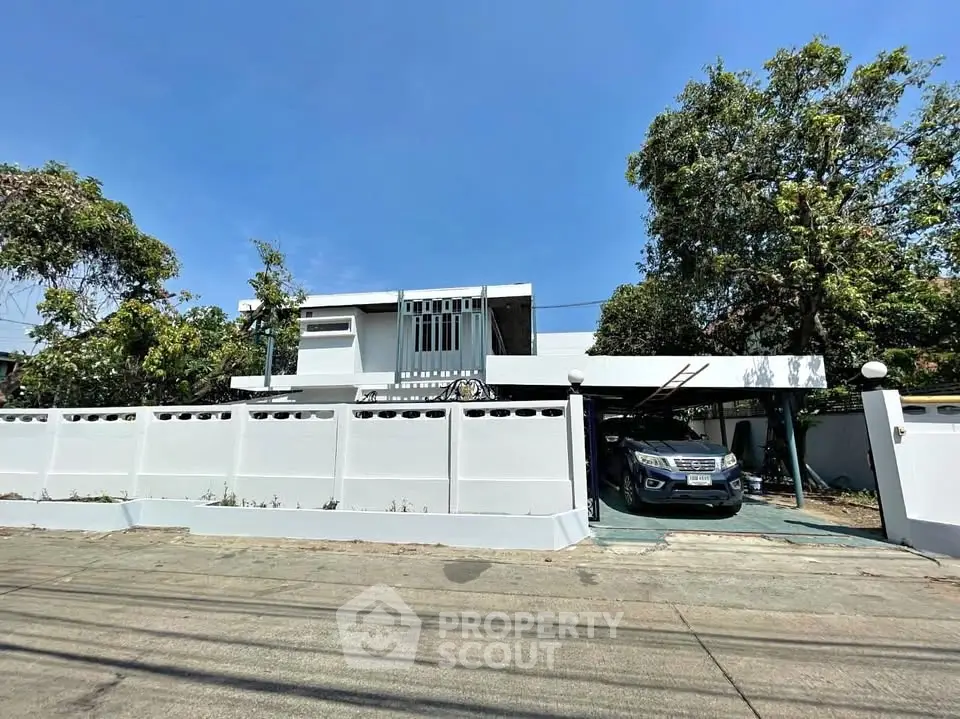 Modern white house with carport and lush greenery in a serene neighborhood.
