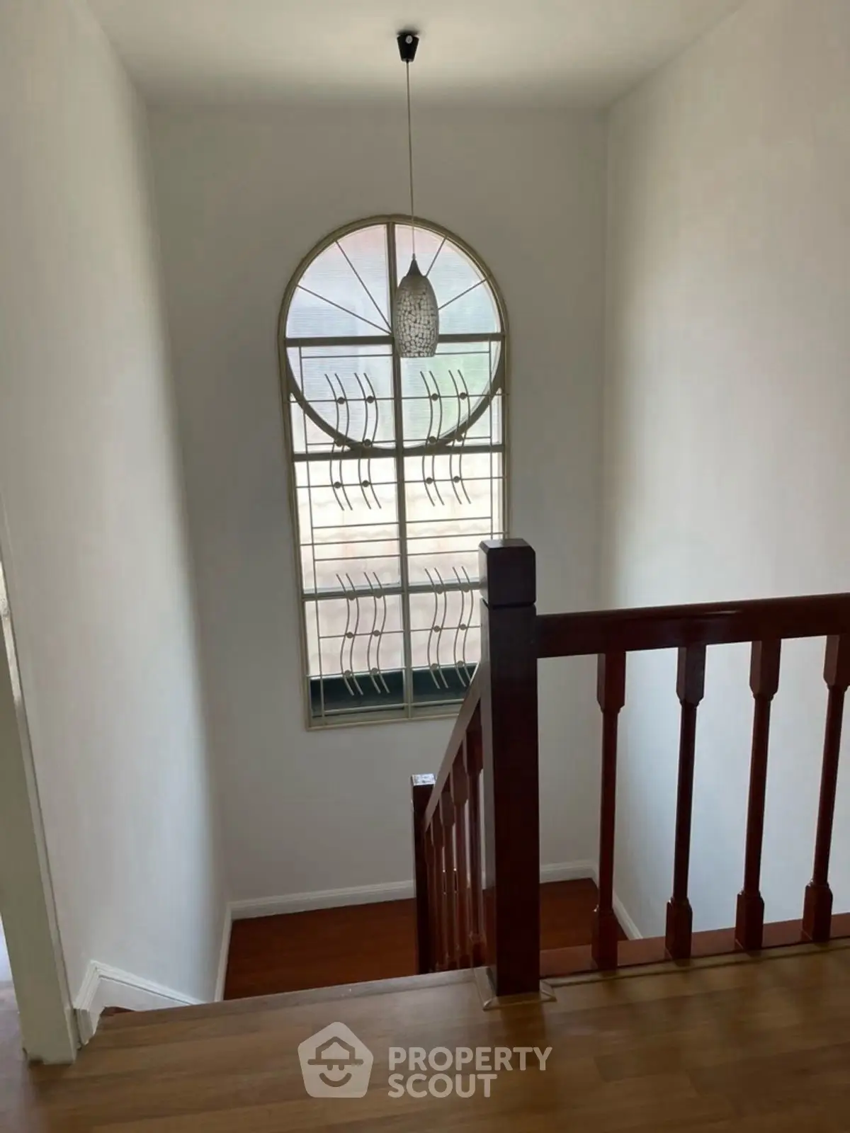 Elegant staircase with wooden railing and arched window in a bright home interior.