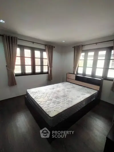 Spacious bedroom with large windows and elegant curtains, featuring a comfortable bed and wooden flooring.