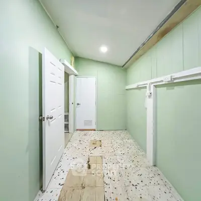 Spacious utility room with mint green walls and terrazzo flooring, featuring white doors and ample lighting.