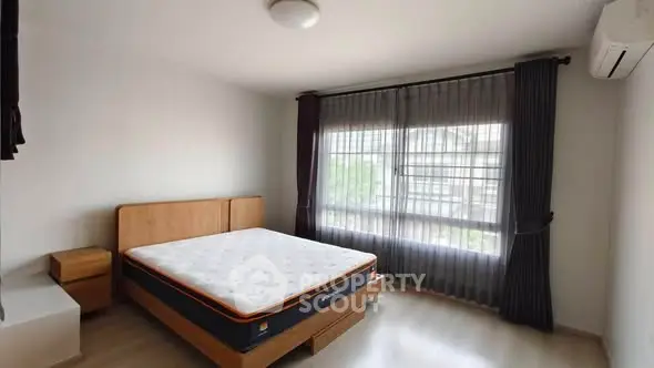Spacious bedroom with large window and modern furnishings in a well-lit apartment.