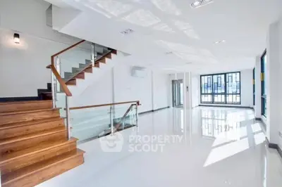 Spacious and modern living area with gleaming white floors, elegant wooden staircase, and abundant natural light from large windows, perfect for upscale urban living.
