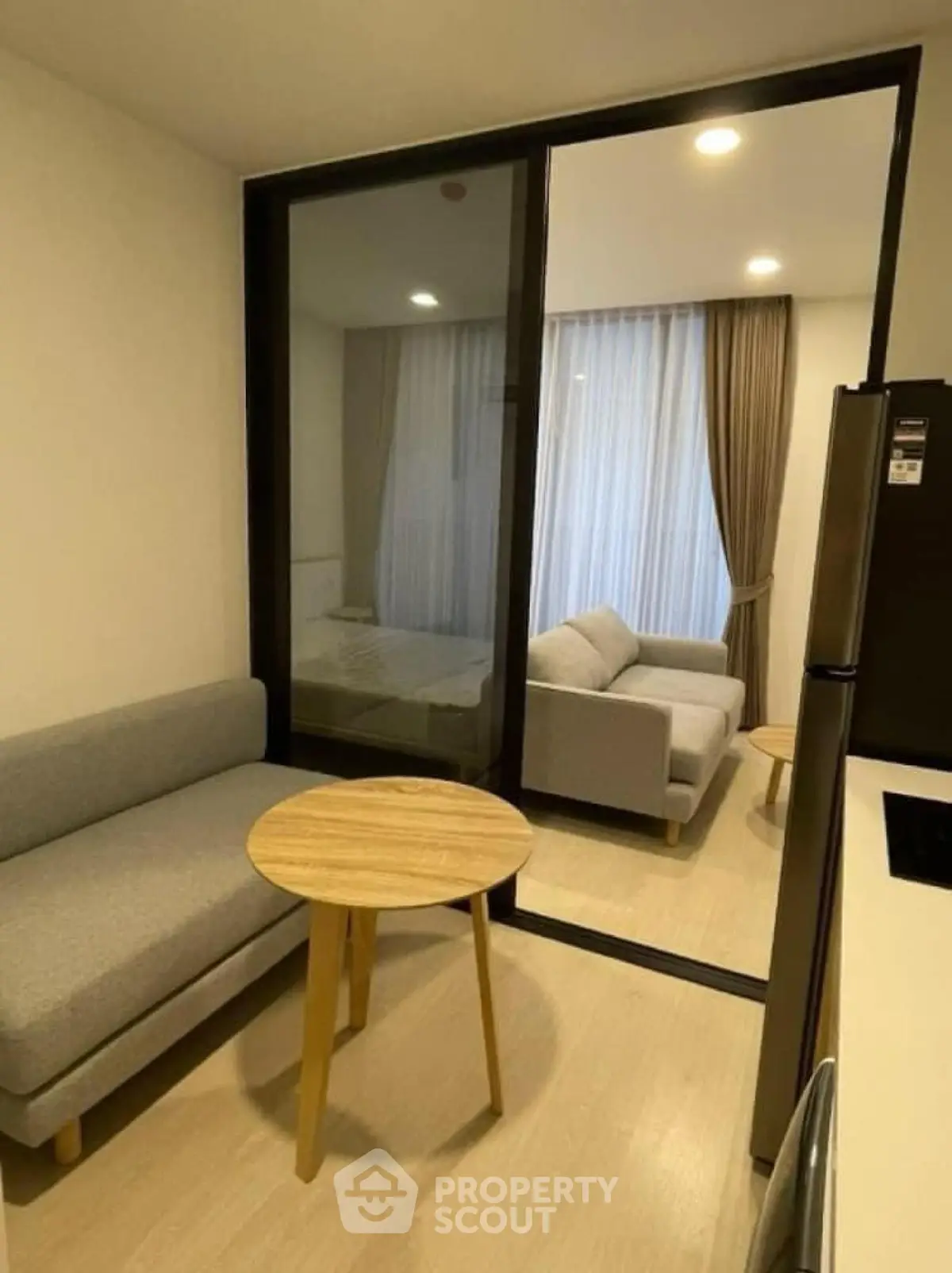 Modern apartment interior with cozy living room and bedroom separated by glass partition, featuring stylish furniture.