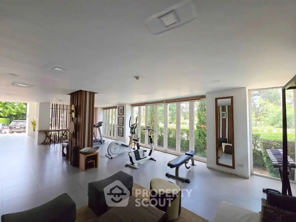 Spacious gym with modern equipment and large windows offering garden views.