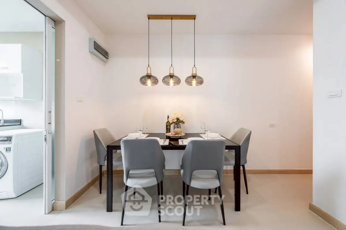 Modern dining area with elegant lighting and adjacent laundry space in a stylish apartment.