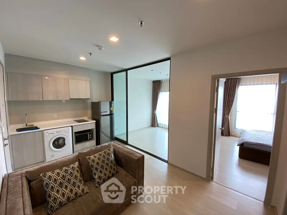 Modern apartment interior with open kitchen and cozy living area, featuring a washing machine and stylish decor.