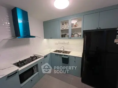 Modern kitchen with blue cabinets, gas stove, and black fridge in sleek design.