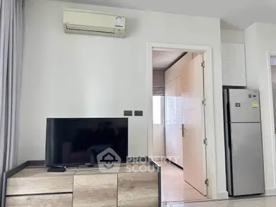 Modern living room with TV and air conditioning, adjacent to a kitchen with stainless steel fridge.