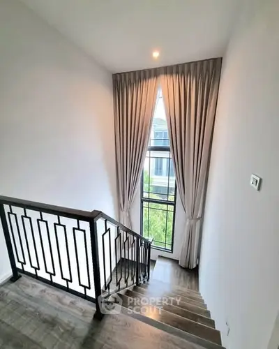 Elegant staircase with large window and modern railing in a bright home interior.