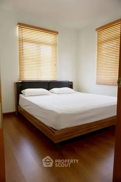 Cozy bedroom with wooden flooring and large windows for natural light.