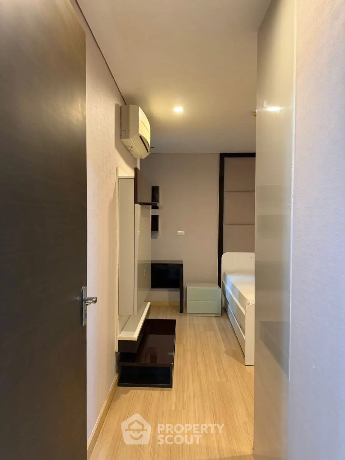 Modern minimalist bedroom with sleek design and wooden flooring, featuring built-in storage and air conditioning.