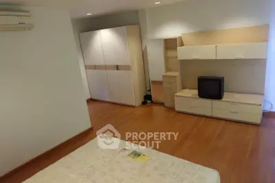 Spacious bedroom with modern furniture and wooden flooring, featuring a cozy ambiance.