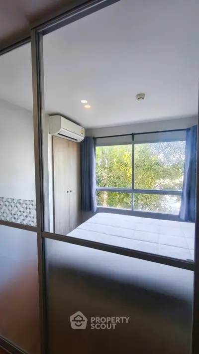 Modern bedroom with large windows and air conditioning, offering a serene view of greenery.