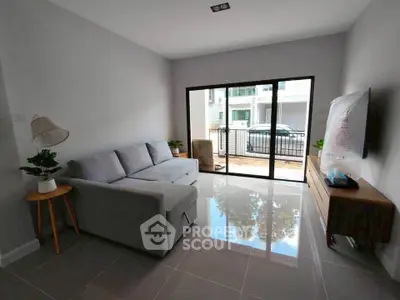 Modern living room with sleek gray sofa and large sliding glass doors opening to balcony.