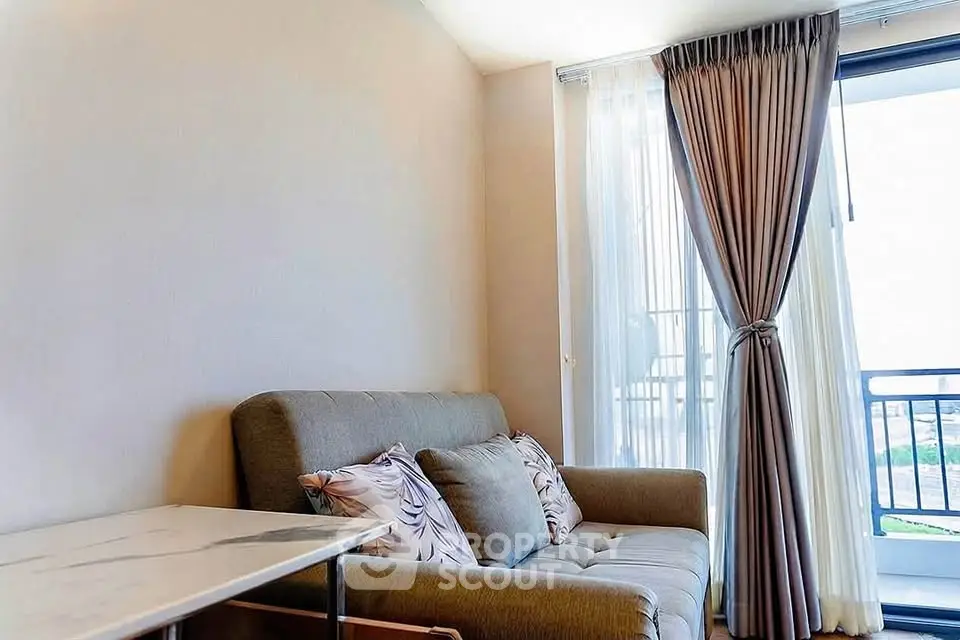 Cozy living room with plush sofa and elegant curtains opening to a balcony with a view.