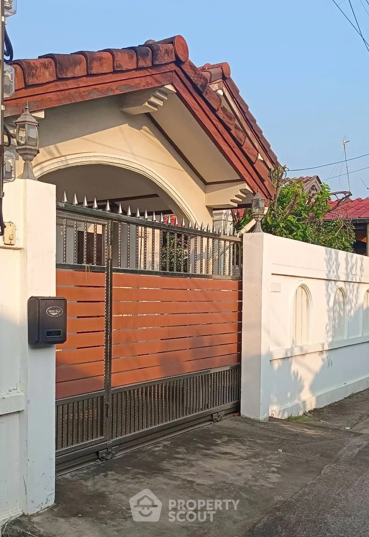 Charming suburban house with red-tiled roof and secure gated entrance.