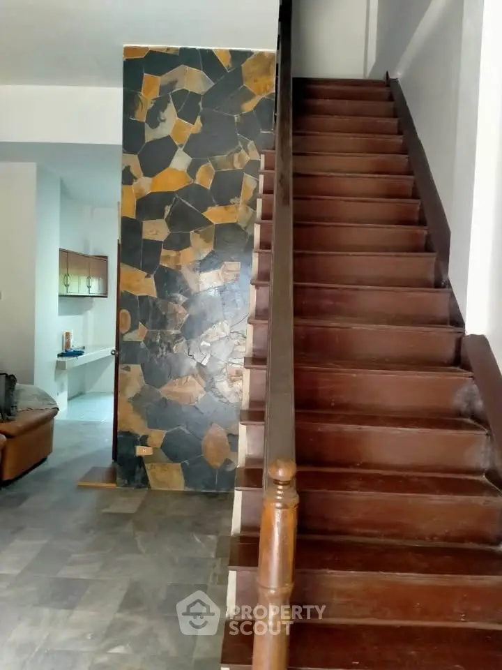 Charming interior with wooden staircase and unique stone accent wall in a cozy living space.