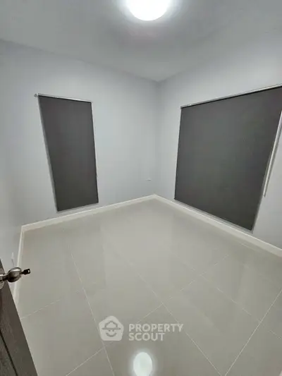 Spacious empty room with sleek tiled flooring and modern window blinds, perfect for customization.