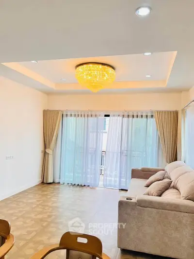 Spacious living room with elegant chandelier and large windows for natural light.