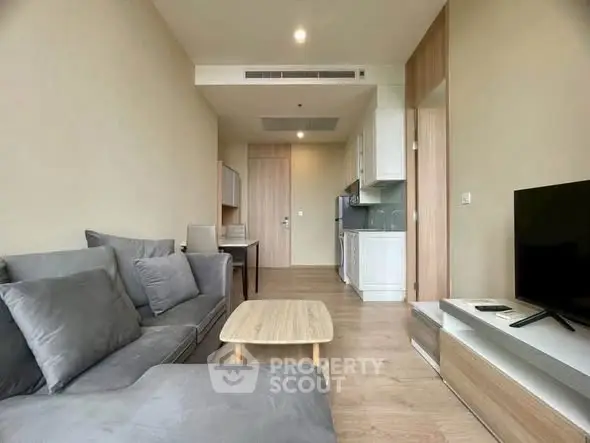 Modern living room with cozy gray sofa, wooden flooring, and open kitchen layout in a stylish apartment.